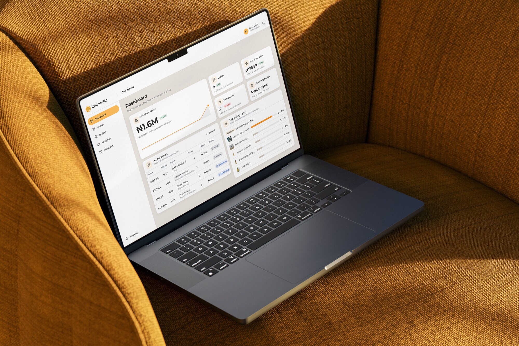 A laptop open on a mustard armchair, showing the QRCodeFlip admin dashboard: today's net sales, orders, menu views, the busiest QR point, recent orders and the top-selling drinks